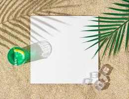 Creative layout of green refreshing drink with lemon slice, palm tree leaf, ice cubes, tropical leaf shadow and paper card note copy space on beach sand background. Minimal exotic summer concept. photo