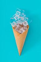 Ice cream cone with ice cubes on aqua blue background. Minimal summer creative concept. Summer food aesthetic. Flat lay, top of view. photo