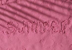 The word Summer handwritten on pink sand surface with tropical palm tree leaf shadow. Minimal concept photo of summer vacation. Sun and shadows. Exotic flat lay. Summer aesthetic.