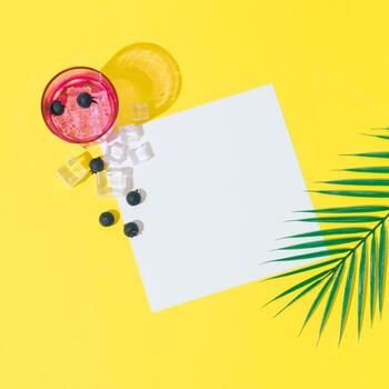 Summer layout made with cold refreshing drink, blueberries, ice cubes, tropical palm leaf and paper card note copy space on yellow background. Minimal concept. Summertime party idea. Flat lay. photo