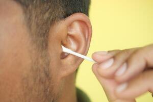 Closeup of young man using ear cotton bar photo