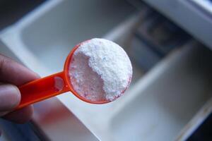 Washing powder in plastic spoon on black background top view. photo