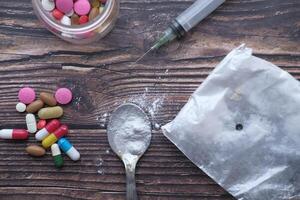 heroine, syringe and pills on wooden background . photo