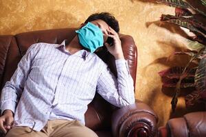 A sick man with a mask on his face resting on sofa photo