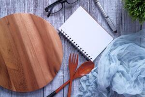 Notepad and chopping board with wooden fork and spoon on white table. photo