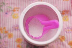 Washing powder in plastic spoon on blue background photo