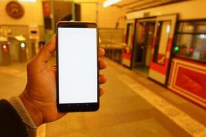 joven hombre mano utilizando inteligente teléfono con blanco pantalla dentro de metro estación foto