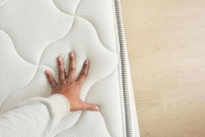 Hand touching and pressing orthopedic mattress on bed. photo