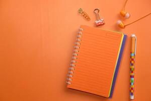 notepad, headphone, pen and office suppliers orange background on photo