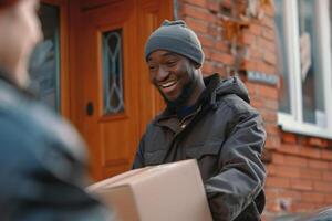 A man wearing a black jacket and a gray hat is smiling as he holds a brown box photo