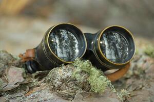 Aged binoculars with a leather strap resting in forest setting photo