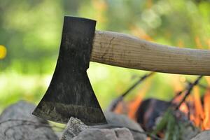 Hatchet embedded in a log of wood opposite campfire photo