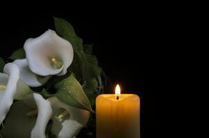 White calla lily flowers and burning wax candle in darkness photo