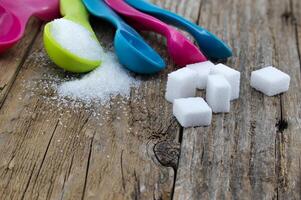 Sugar in colorful measuring spoons on wooden surface photo