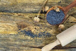 Poppy seeds and several dried poppy seed pods on wooden table photo