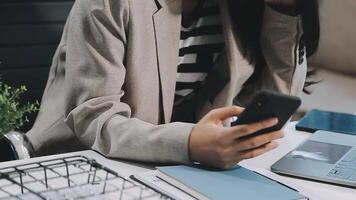 Asian woman entrepreneur busy with her work in the office. Young Asian woman work on desk laptop phone while planning sales, research or financial strategy in company video