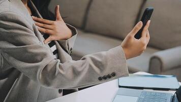 Asian woman entrepreneur busy with her work in the office. Young Asian woman work on desk laptop phone while planning sales, research or financial strategy in company video