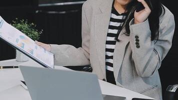 Asian woman entrepreneur busy with her work in the office. Young Asian woman work on desk laptop phone while planning sales, research or financial strategy in company video