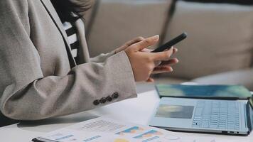 Asian woman entrepreneur busy with her work in the office. Young Asian woman work on desk laptop phone while planning sales, research or financial strategy in company video