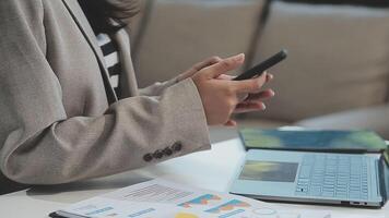 Asian woman entrepreneur busy with her work in the office. Young Asian woman work on desk laptop phone while planning sales, research or financial strategy in company video