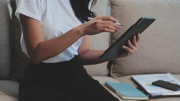 Asian woman entrepreneur busy with her work in the office. Young Asian woman work on desk laptop phone while planning sales, research or financial strategy in company video