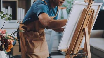 Over the shoulder selective focus shot of male artist using brush while adding color paint to pencil drawing on canvas video