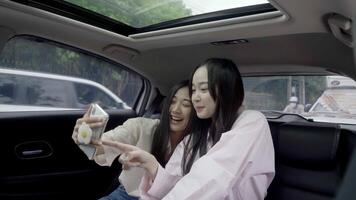 Two girlfriends in backseat of car taking selfie with a smart phone. Girl smiling and posing to photo video