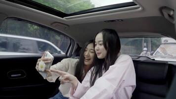 Due amiche nel sedile posteriore di auto assunzione autoscatto con un' inteligente Telefono. ragazza sorridente e in posa per foto video