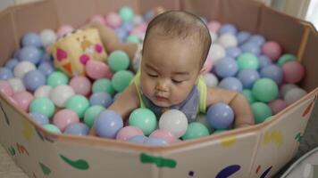 een baby is spelen met een bal in een zwembad van ballen. de baby is omringd door een veel van ballen, en het lijkt Leuk vinden de baby is hebben een veel van pret video