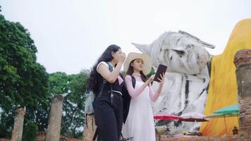 zwei asiatisch Frauen sind Rucksacktouristen reisen. beim ein Buddhist Tempel Ayutthaya im Thailand Lebensstil ist Das Touristen aussehen sehr glücklich. Lächeln und haben Spaß während auf Urlaub. video