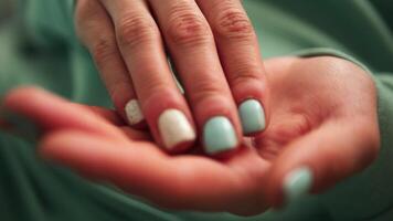 This shows female hands close-up, fingers delicately taking pills from palm green color of clothes and nails adds striking contrast, emphasizing pills and the careful handling of medication. video