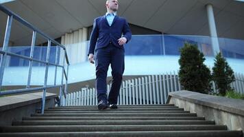 A Businessman descends stairs gracefully in sharp attire. Each step showcases the Businessman's poise. Background office building Businessman's movement reflects professional elegance Business Concept video