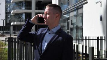 A Businessman engages in a phone conversation outside an office building, dressed in formal business attire. The Businessman's professional demeanor is evident as he discusses important matters. video