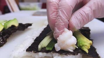 Japonais cuisine chef en train de préparer une rouleau avec fromage, concombre, et Avocat. le chef soigneusement pose vers le bas crevette sur le rouleau, mettant en valeur le complexe processus de fabrication une délicieux Sushi rouleau. video