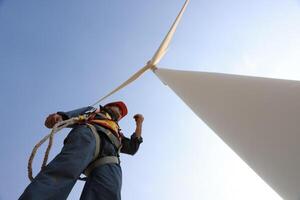 Specialist wind turbine technician working at the base of the turbine. Wind turbine service technician wearing safety uniform and safety harness working at windmill farm photo