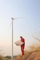 windmill engineer with red safety uniform hold drawing work at front of wind turbine farm photo