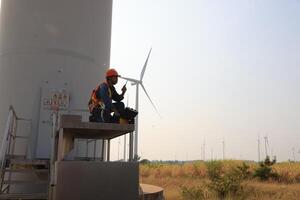 Specialist wind turbine technician working at the base of the turbine. Wind turbine service technician wearing safety uniform and safety harness working at windmill farm photo