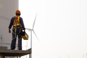 Specialist wind turbine technician working at the base of the turbine. Wind turbine service technician wearing safety uniform and safety harness working at windmill farm photo