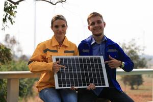 Male and female energy engineers holding a small solar panel together at the windmill photo