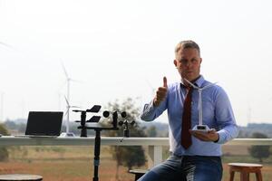 A senior male energy specialist is inspecting wind turbines on an ecological construction project using a wind speed measuring instrument at a windmill. photo