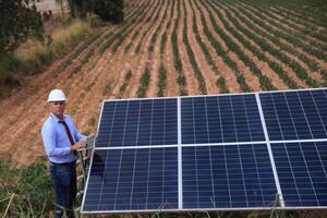 A senior male engineer inspects solar panels on the windmill farm. Clean energy. Engineers inspect a solar panel system with a turbine farm in the background, a renewable energy concept photo