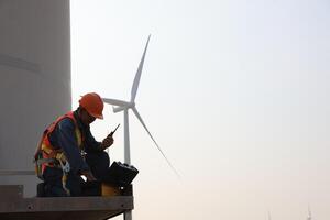 Specialist wind turbine technician working at the base of the turbine. Wind turbine service technician wearing safety uniform and safety harness working at windmill farm photo