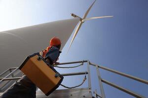 Specialist wind turbine technician working at the base of the turbine. Wind turbine service technician wearing safety uniform and safety harness working at windmill farm photo