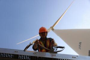 Specialist wind turbine technician working at the base of the turbine. Wind turbine service technician wearing safety uniform and safety harness working at windmill farm photo