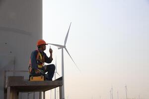 Specialist wind turbine technician working at the base of the turbine. Wind turbine service technician wearing safety uniform and safety harness working at windmill farm photo