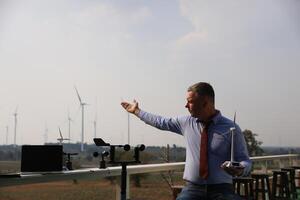 A senior male energy specialist is inspecting wind turbines on an ecological construction project using a wind speed measuring instrument at a windmill. photo