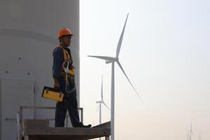 Specialist wind turbine technician working at the base of the turbine. Wind turbine service technician wearing safety uniform and safety harness working at windmill farm photo