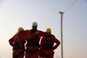 Portrait Windmill engineer team with red work uniform with safety hard hat and harness work in wind turbine farm photo