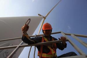 Specialist wind turbine technician working at the base of the turbine. Wind turbine service technician wearing safety uniform and safety harness working at windmill farm photo