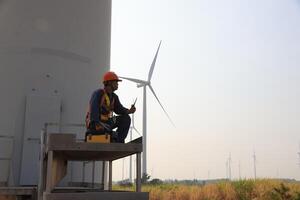 Specialist wind turbine technician working at the base of the turbine. Wind turbine service technician wearing safety uniform and safety harness working at windmill farm photo